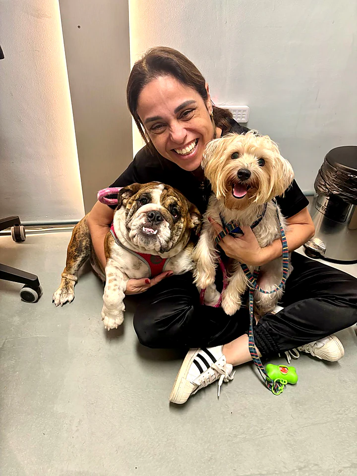 Colaboradora sentada no chão abraçando dois cães pequenos